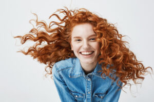 Portrait of beautiful happy cheerful redhead girl with flyingcurly hair smiling laughing looking at camera over white background.